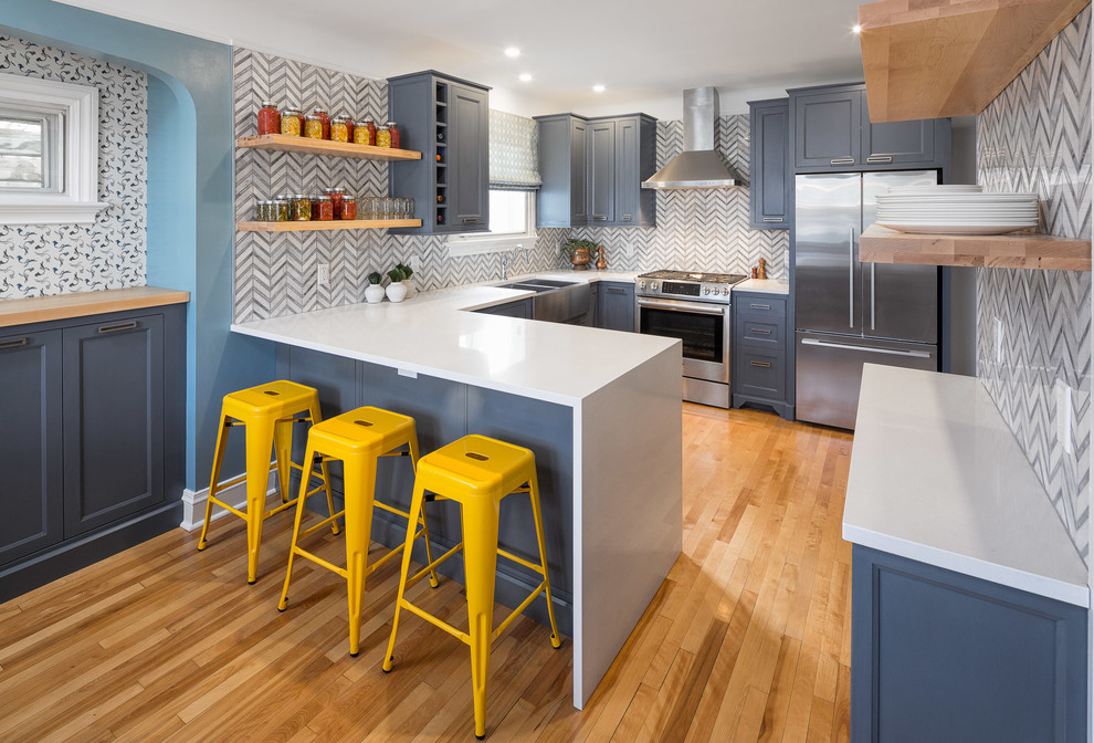This is an example of a mid-sized transitional u-shaped kitchen in Ottawa with recessed-panel cabinets, blue cabinets, quartzite benchtops, grey splashback, stone tile splashback, stainless steel appliances, medium hardwood floors, a farmhouse sink and no island.