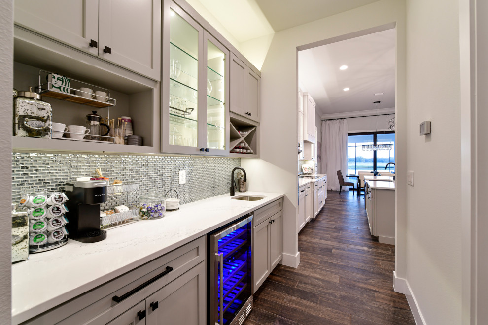 Inspiration for a mid-sized transitional l-shaped porcelain tile and brown floor eat-in kitchen remodel with a farmhouse sink, shaker cabinets, white cabinets, quartz countertops, metallic backsplash, glass tile backsplash, stainless steel appliances, an island and white countertops