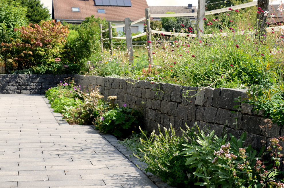 Cette image montre un grand jardin latéral design l'été avec un mur de soutènement, une exposition ensoleillée et des pavés en béton.