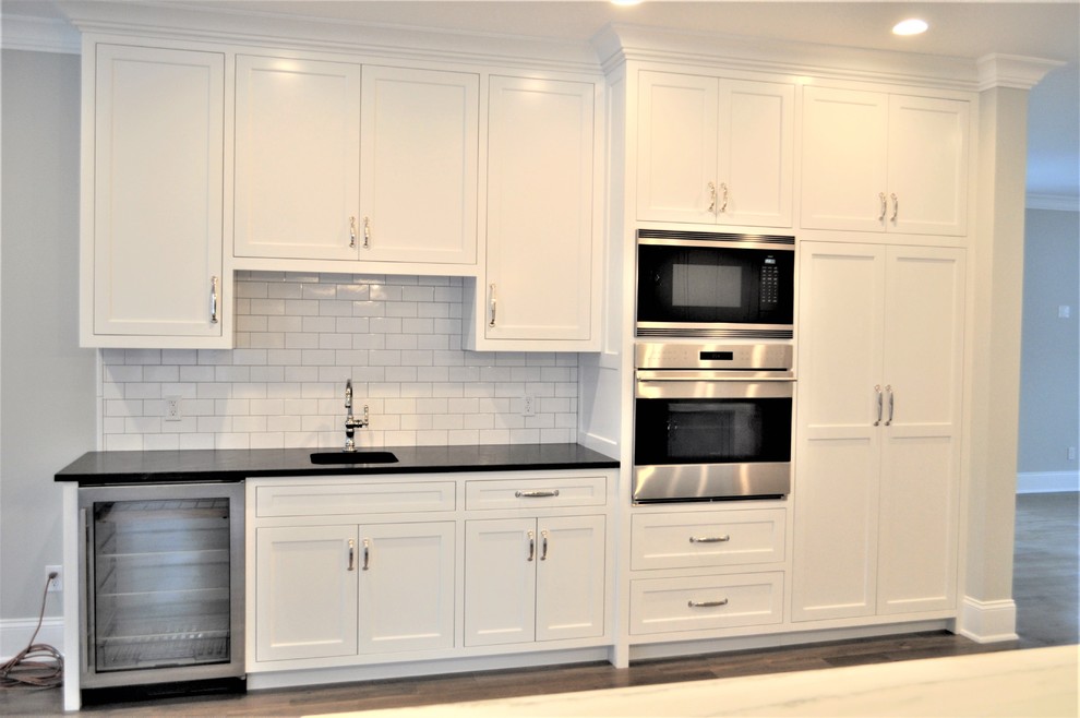 Inspiration for a transitional light wood floor and gray floor kitchen remodel with a single-bowl sink, shaker cabinets, white cabinets, marble countertops, white backsplash, subway tile backsplash, stainless steel appliances, an island and black countertops