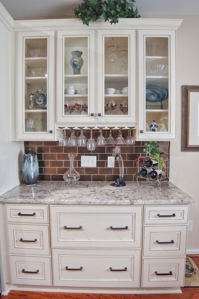 Example of a mid-sized u-shaped medium tone wood floor and brown floor kitchen design in Charleston with an undermount sink, raised-panel cabinets, beige cabinets, granite countertops, brown backsplash, ceramic backsplash, stainless steel appliances and beige countertops