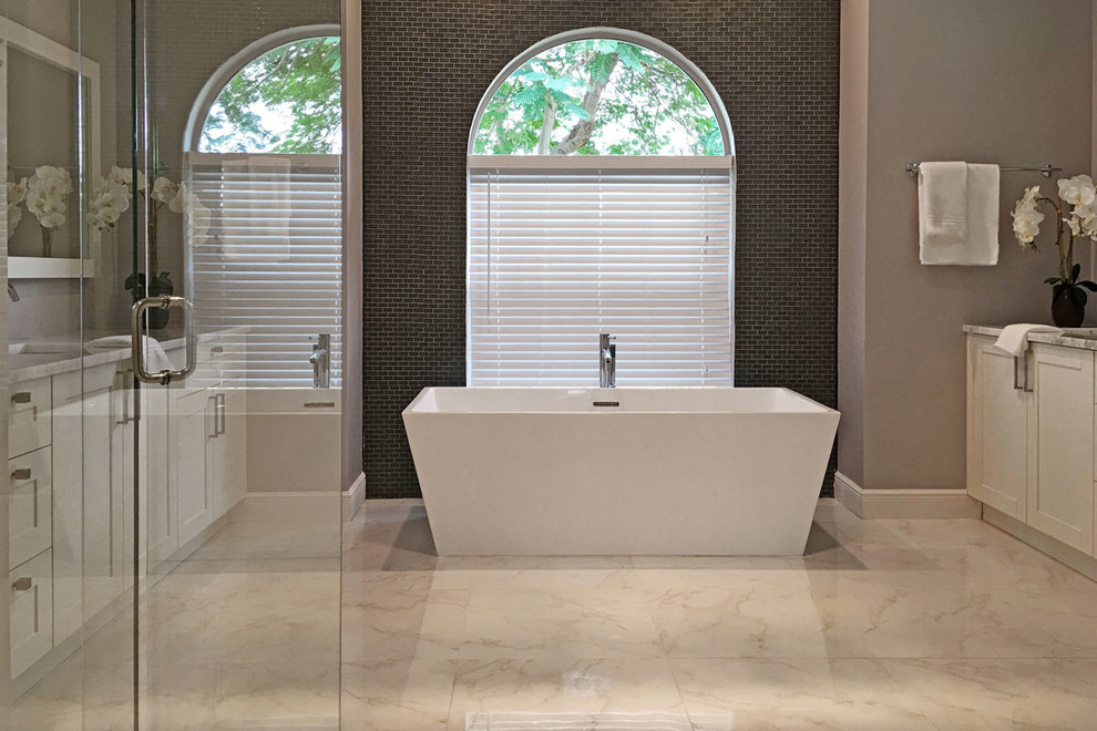Photo of a large contemporary master bathroom in Tampa with recessed-panel cabinets, white cabinets, a freestanding tub, an alcove shower, a one-piece toilet, black tile, porcelain tile, grey walls, marble floors, an undermount sink, marble benchtops, white floor and a hinged shower door.