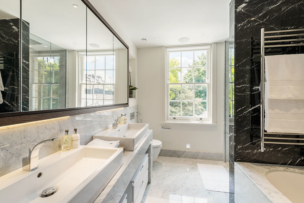 Design ideas for a contemporary bathroom in London with a console sink, marble benchtops, an undermount tub, a double shower, a wall-mount toilet, stone slab, marble floors, flat-panel cabinets and white cabinets.