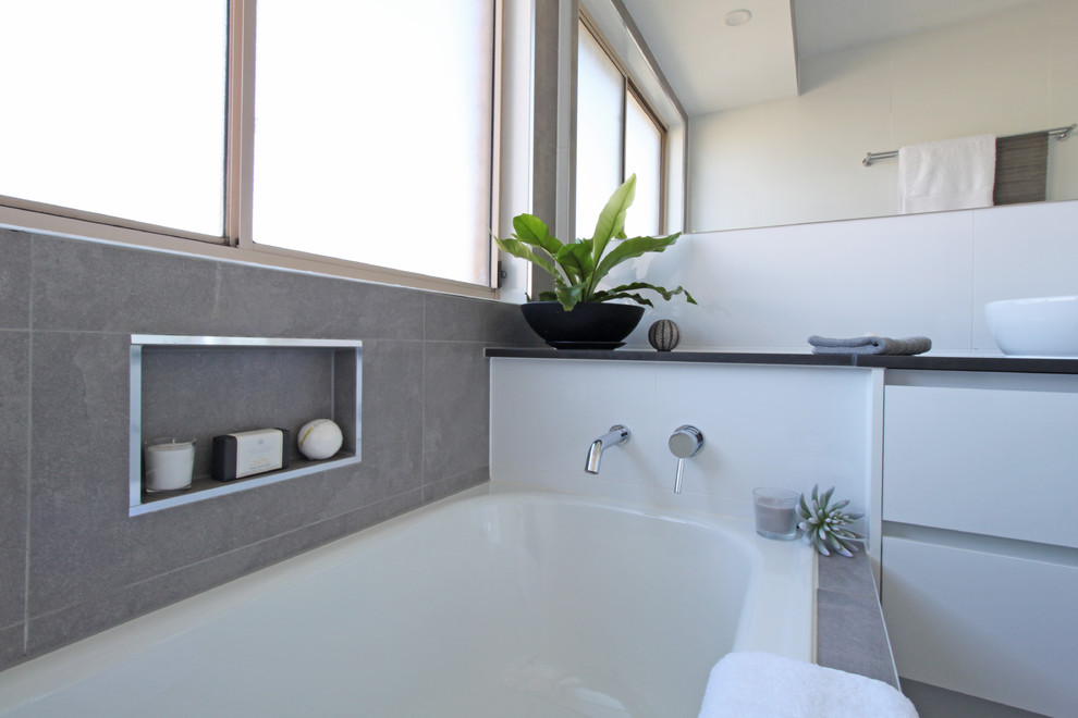 Design ideas for a small contemporary kids bathroom in Brisbane with flat-panel cabinets, white cabinets, a drop-in tub, a corner shower, a two-piece toilet, white tile, ceramic tile, white walls, terra-cotta floors, a vessel sink, engineered quartz benchtops, grey floor, a hinged shower door and black benchtops.