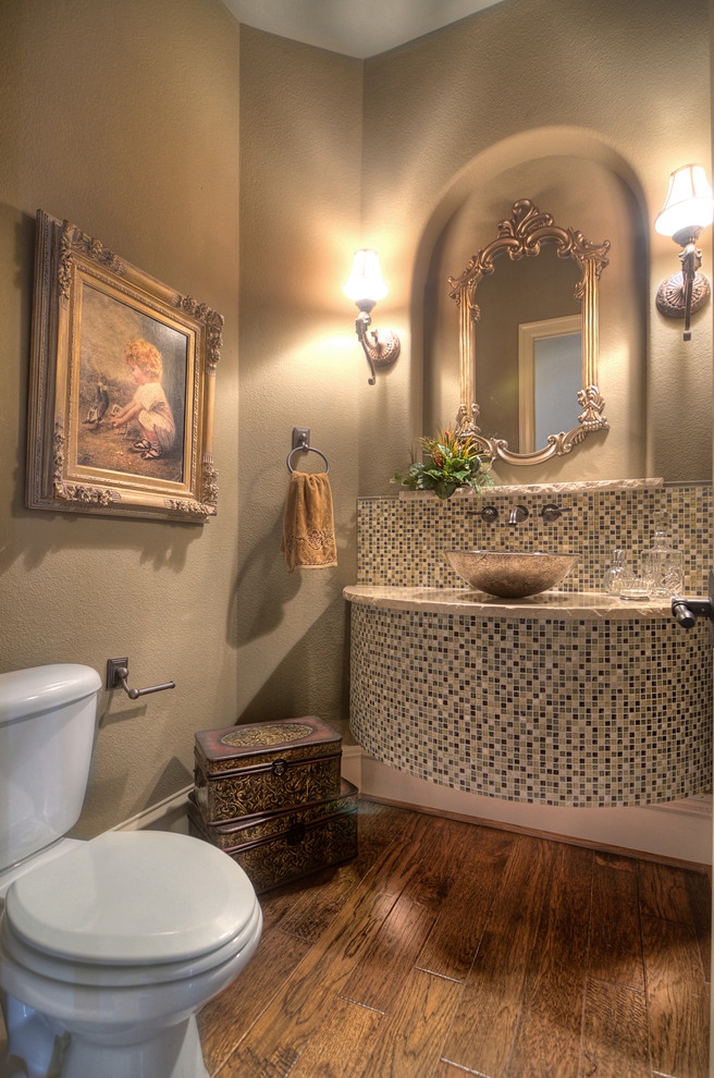 Photo of a large mediterranean powder room in Houston with a one-piece toilet, brown tile, glass sheet wall, beige walls, medium hardwood floors, a vessel sink and granite benchtops.