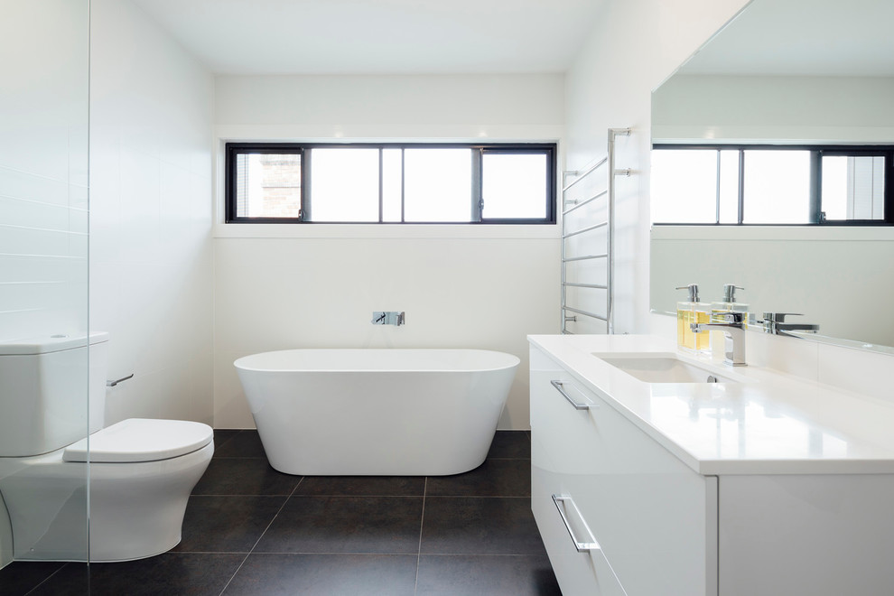 This is an example of a small contemporary bathroom in Sydney with flat-panel cabinets, white cabinets, a freestanding tub, an open shower, a two-piece toilet, white tile, porcelain tile, white walls, slate floors, an undermount sink and limestone benchtops.