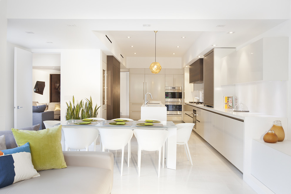Photo of a contemporary u-shaped open plan kitchen in Miami with an undermount sink, white splashback, porcelain splashback, stainless steel appliances, porcelain floors, flat-panel cabinets, white cabinets, with island and white floor.