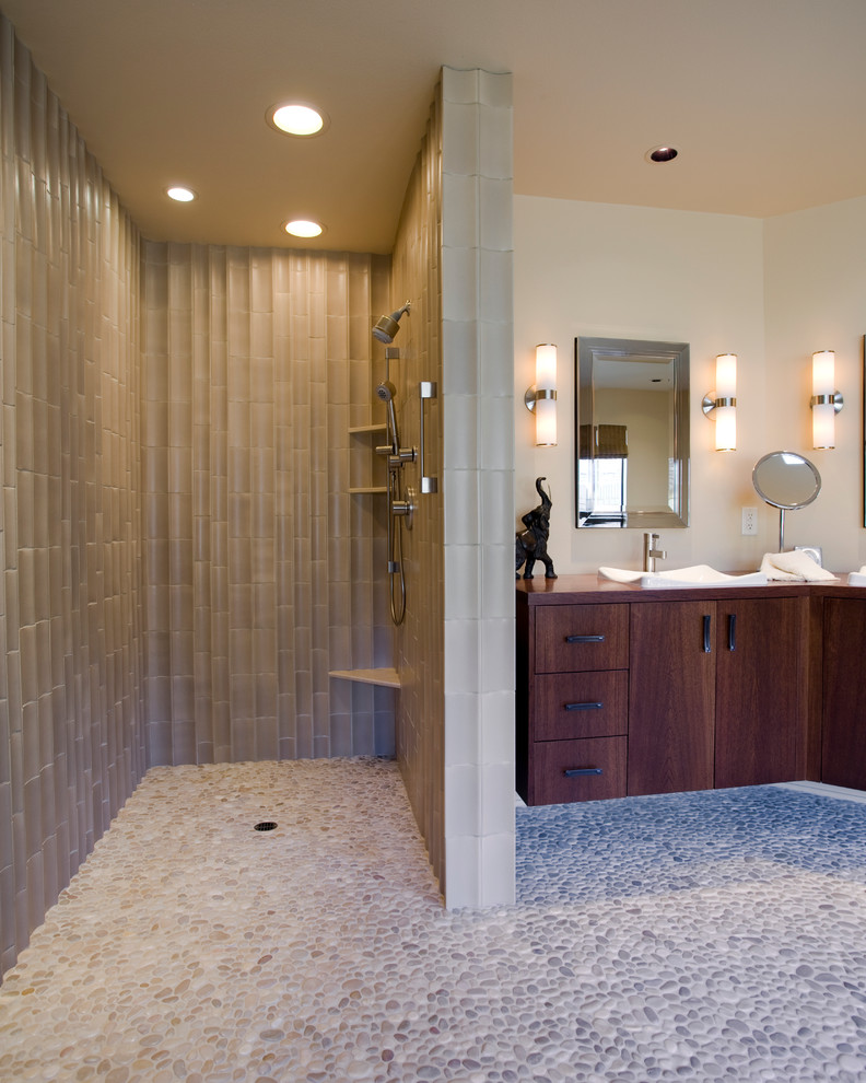 This is an example of a transitional bathroom in Portland with a vessel sink, flat-panel cabinets, dark wood cabinets, wood benchtops, an open shower, beige tile, porcelain tile, pebble tile floors, an open shower and brown benchtops.