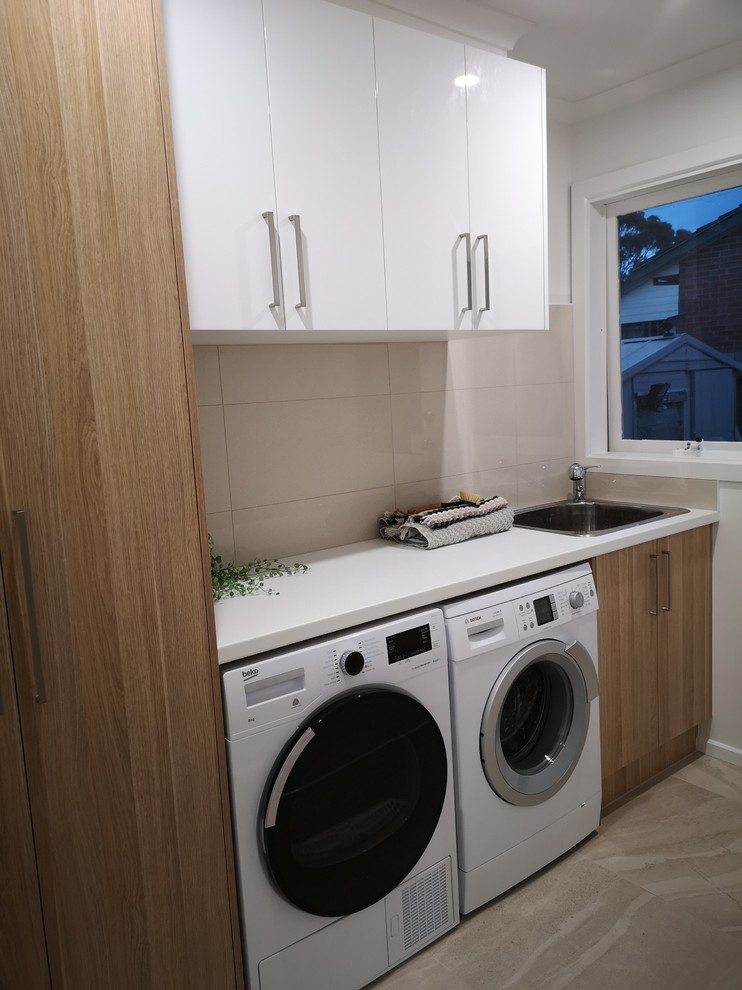 Inspiration for a small modern single-wall dedicated laundry room in Melbourne with a drop-in sink, recessed-panel cabinets, light wood cabinets, laminate benchtops, beige walls, porcelain floors, a side-by-side washer and dryer, beige floor and white benchtop.