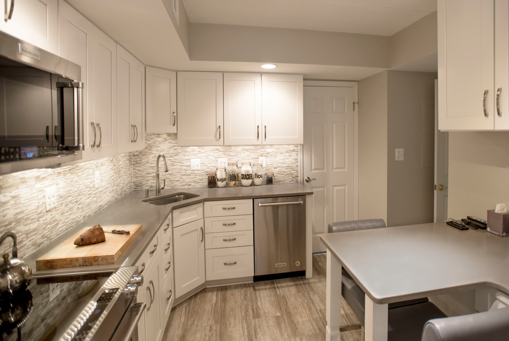 Example of a mid-sized transitional l-shaped ceramic tile kitchen pantry design in Baltimore with a drop-in sink, shaker cabinets, white cabinets, quartz countertops, gray backsplash, glass sheet backsplash, stainless steel appliances and a peninsula