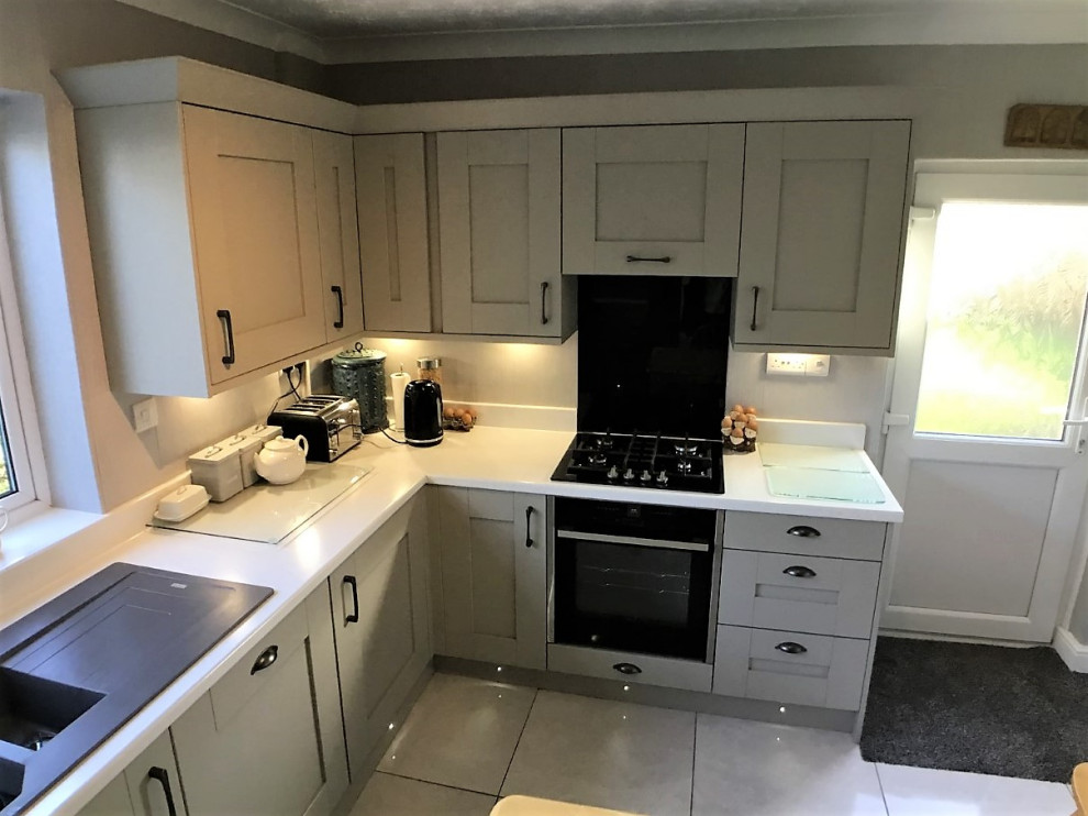 Klassisk inredning av ett mellanstort vit vitt kök och matrum, med skåp i shakerstil, laminatbänkskiva, svart stänkskydd, glaspanel som stänkskydd, svarta vitvaror och grått golv
