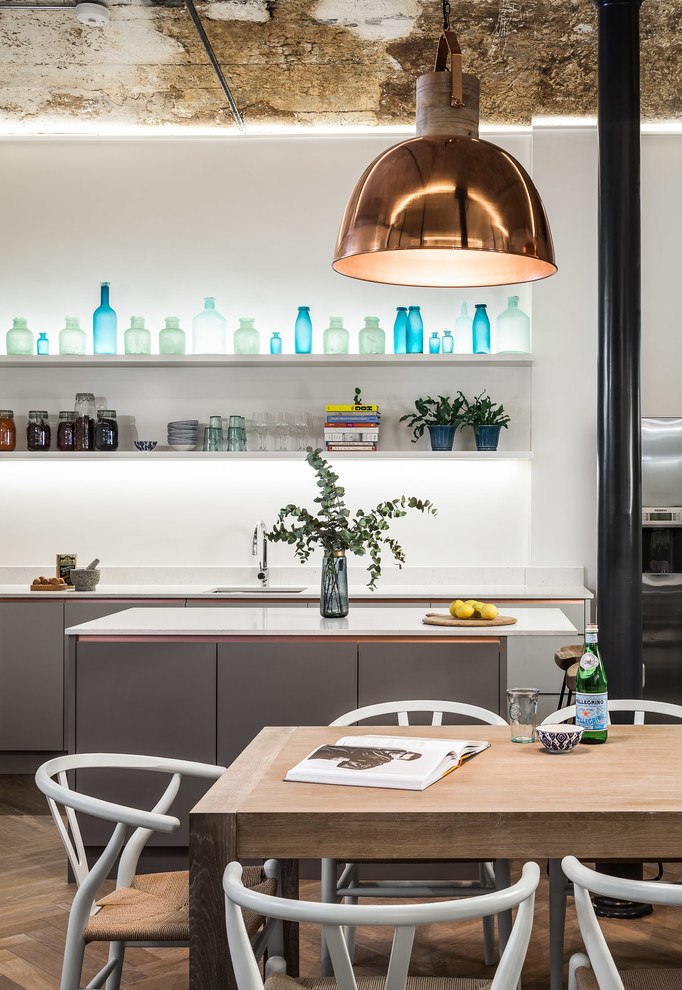 Design ideas for an industrial open plan kitchen in London with an undermount sink, grey cabinets, solid surface benchtops, white splashback, stainless steel appliances, light hardwood floors and with island.
