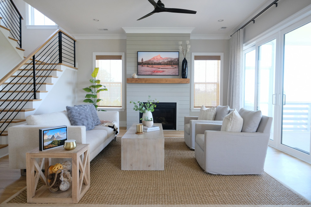 This is an example of a mid-sized beach style open concept living room in Charleston with grey walls, medium hardwood floors, a standard fireplace and a wall-mounted tv.