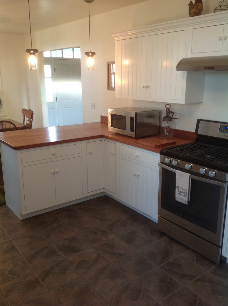 Example of a mid-sized l-shaped medium tone wood floor enclosed kitchen design with a farmhouse sink, flat-panel cabinets, white cabinets, wood countertops, beige backsplash, stainless steel appliances and no island