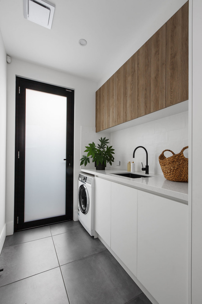 Design ideas for a contemporary single-wall laundry room in Melbourne with an undermount sink, flat-panel cabinets, white cabinets, white splashback, white walls, an integrated washer and dryer, grey floor and white benchtop.