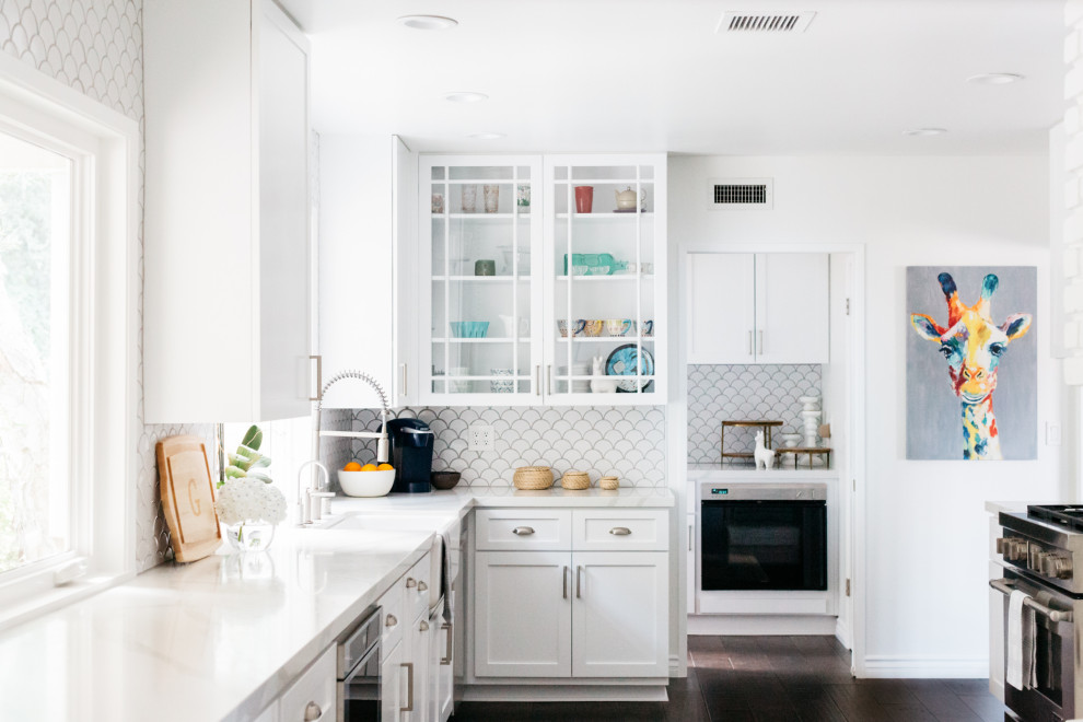 Photo of a transitional u-shaped kitchen in Los Angeles with a farmhouse sink, shaker cabinets, white cabinets, stainless steel appliances, dark hardwood floors, no island, brown floor and white benchtop.