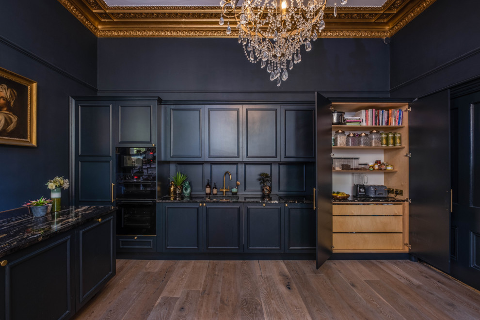 Inspiration for a large traditional single-wall eat-in kitchen in Sussex with a drop-in sink, beaded inset cabinets, blue cabinets, granite benchtops, blue splashback, timber splashback, black appliances, light hardwood floors, with island, brown floor, black benchtop and coffered.