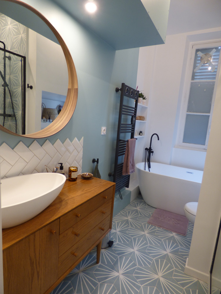 This is an example of a small modern 3/4 bathroom in Lyon with a drop-in tub, an alcove shower, a wall-mount toilet, white tile, ceramic tile, blue walls, ceramic floors, a drop-in sink, wood benchtops, blue floor, a sliding shower screen and beige benchtops.