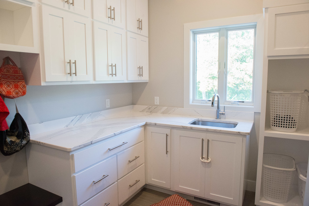 Large transitional l-shaped porcelain tile and gray floor utility room photo with an undermount sink, shaker cabinets, white cabinets, quartz countertops, gray walls and a side-by-side washer/dryer