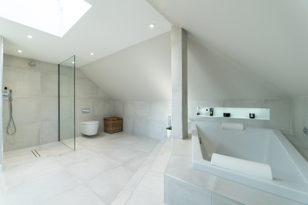 Expansive contemporary master wet room bathroom in Edinburgh with open cabinets, grey cabinets, a drop-in tub, a wall-mount toilet, beige tile, ceramic tile, beige walls, ceramic floors, a vessel sink, glass benchtops, beige floor, an open shower and grey benchtops.