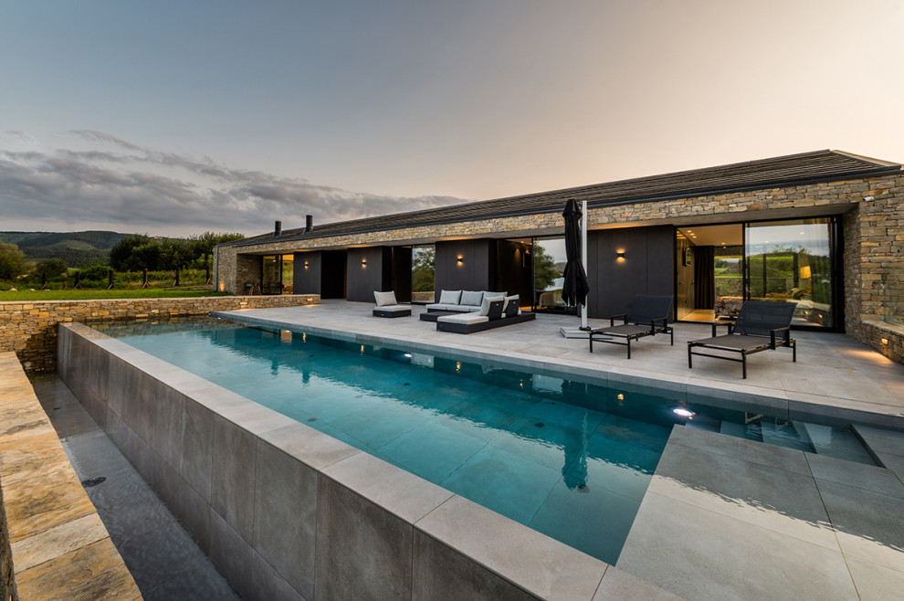 Photo of a large modern rectangular infinity swimming pool in Other with tiled flooring.