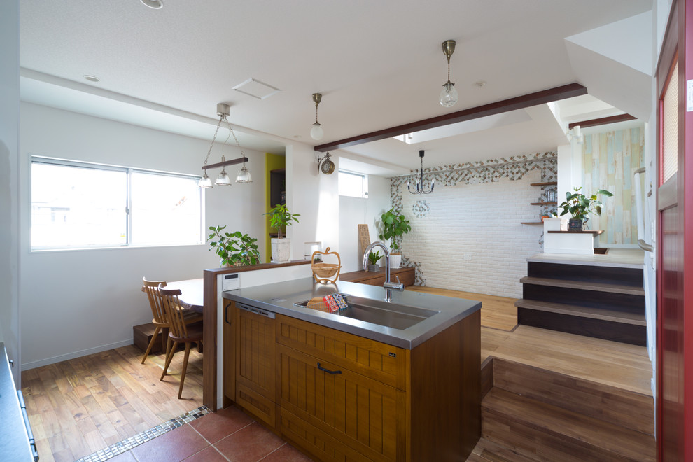 This is an example of a mediterranean kitchen in Kyoto with a single-bowl sink, medium wood cabinets, stainless steel benchtops, terra-cotta floors, with island and red floor.