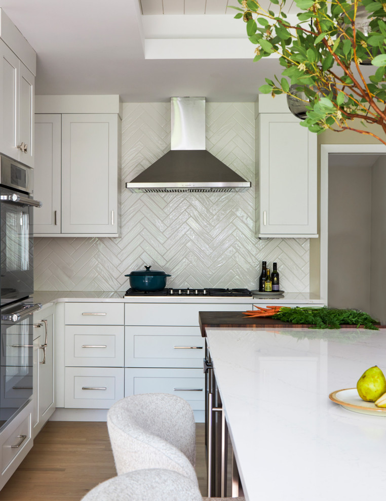 Example of a large transitional u-shaped light wood floor, brown floor and coffered ceiling eat-in kitchen design in Chicago with a farmhouse sink, shaker cabinets, white cabinets, quartz countertops, white backsplash, subway tile backsplash, stainless steel appliances, an island and multicolored countertops