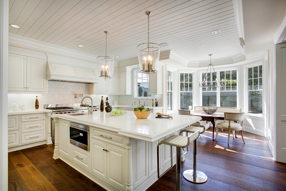 Photo of a traditional eat-in kitchen in Los Angeles with a farmhouse sink, raised-panel cabinets, white cabinets, white splashback, stainless steel appliances, dark hardwood floors and with island.