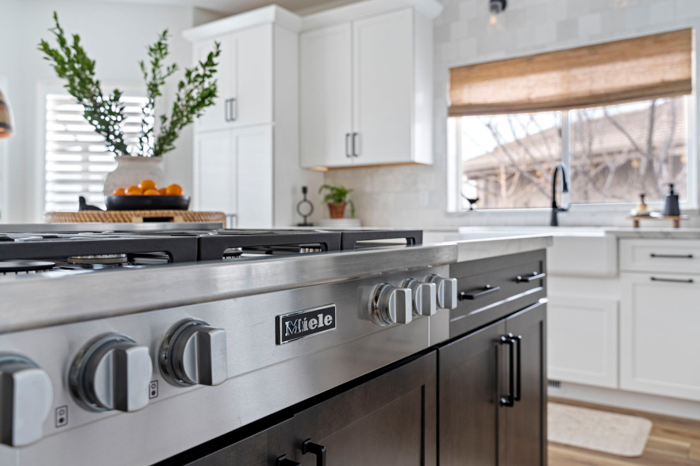 Inspiration for a transitional vinyl floor and brown floor kitchen remodel with a farmhouse sink, shaker cabinets, white cabinets, quartzite countertops, white backsplash and stainless steel appliances
