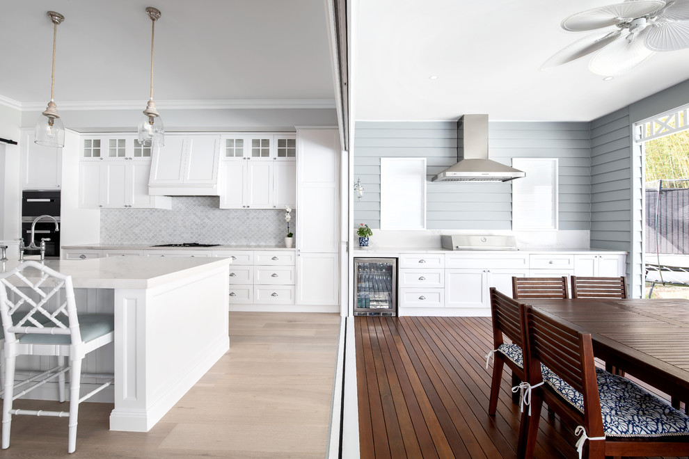 Design ideas for a traditional single-wall kitchen in Gold Coast - Tweed with an undermount sink, shaker cabinets, white cabinets, grey splashback, mosaic tile splashback, black appliances, light hardwood floors, with island, beige floor and white benchtop.