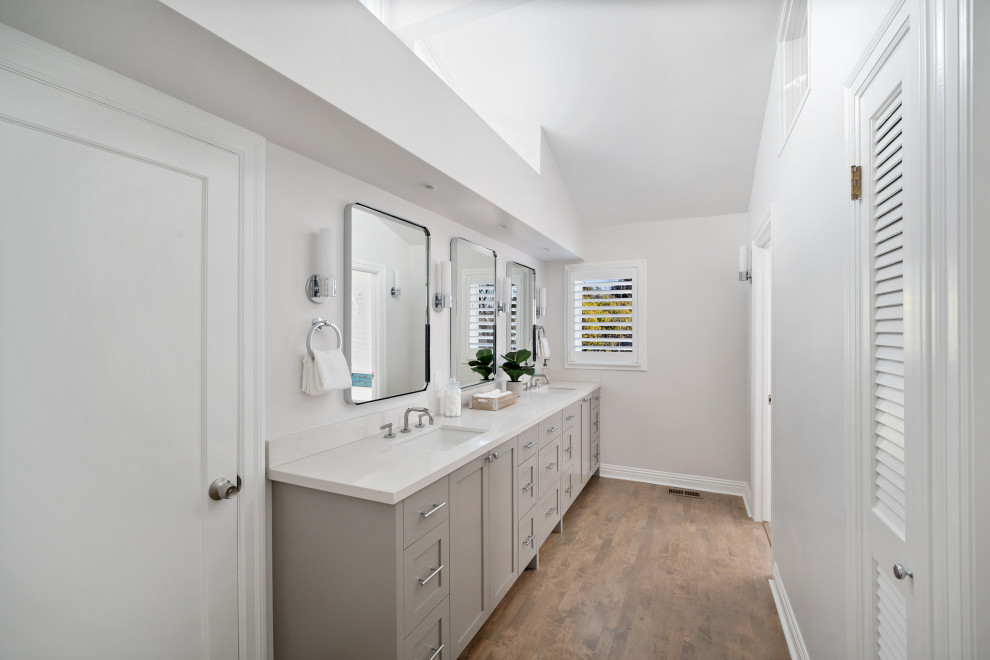 Large traditional ensuite bathroom in San Francisco with shaker cabinets, grey cabinets, white walls, medium hardwood flooring, a submerged sink, engineered stone worktops, brown floors, white worktops, double sinks, a built in vanity unit and a vaulted ceiling.