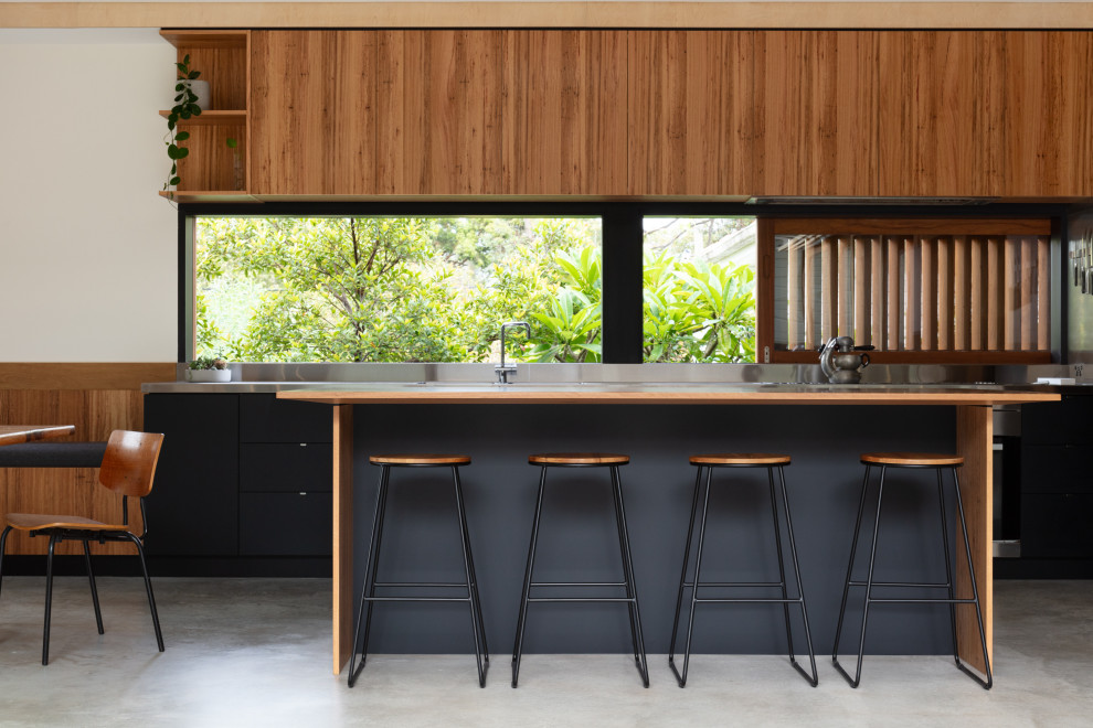 Idéer för ett mellanstort modernt brun kök, med en undermonterad diskho, bruna skåp, bänkskiva i rostfritt stål, fönster som stänkskydd, rostfria vitvaror, betonggolv, en köksö och grått golv