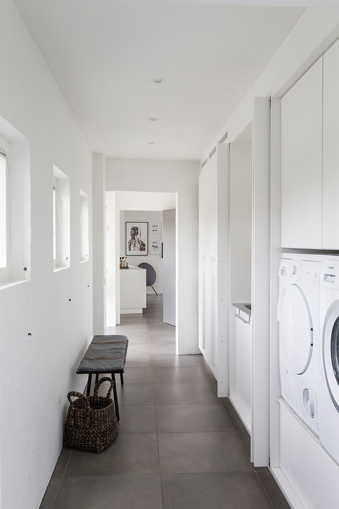 Design ideas for a contemporary laundry room in Other with flat-panel cabinets, white cabinets, white walls, grey floor and a side-by-side washer and dryer.