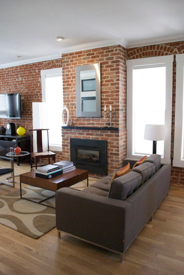 This is an example of a mid-sized modern formal loft-style living room in Denver with white walls, light hardwood floors, a standard fireplace, a brick fireplace surround and a wall-mounted tv.