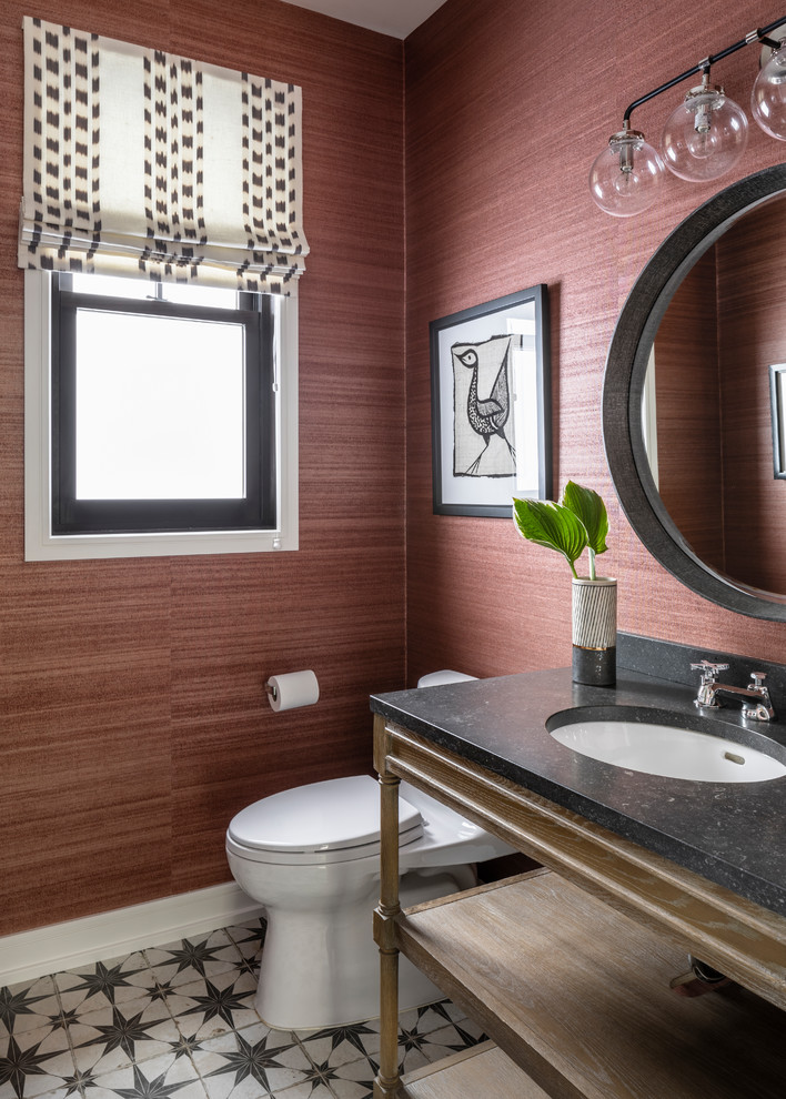 Transitional powder room in New York with open cabinets, a one-piece toilet, red walls, an undermount sink and black benchtops.