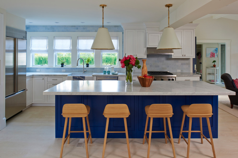 Inspiration for a mid-sized beach style l-shaped eat-in kitchen in New York with a farmhouse sink, recessed-panel cabinets, white cabinets, marble benchtops, blue splashback, ceramic splashback, stainless steel appliances, light hardwood floors and with island.