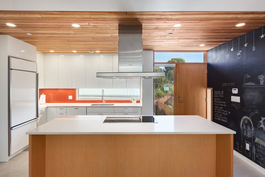 This is an example of a contemporary l-shaped kitchen in Vancouver with an undermount sink, flat-panel cabinets, white cabinets, quartz benchtops, orange splashback, glass sheet splashback, white appliances, concrete floors and with island.