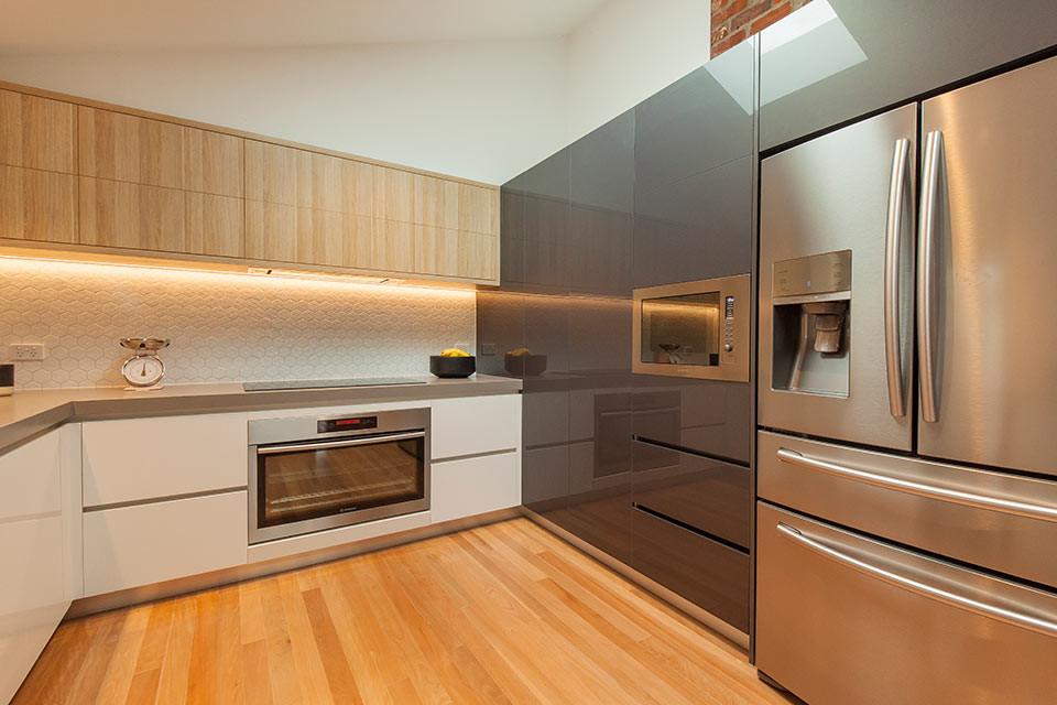 Mid-sized contemporary u-shaped eat-in kitchen in Geelong with a double-bowl sink, white splashback, ceramic splashback, stainless steel appliances, light hardwood floors, no island, flat-panel cabinets, white cabinets and quartz benchtops.