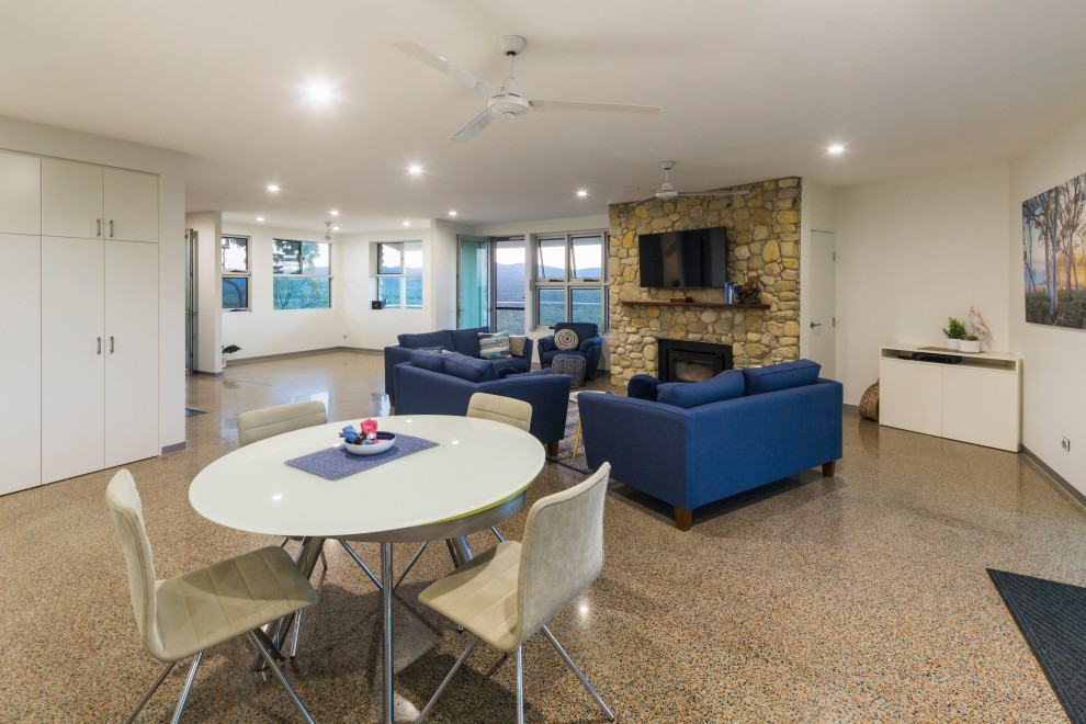 Mid-sized country open concept living room in Cairns with a library, white walls, concrete floors, a wood stove, a stone fireplace surround and white floor.