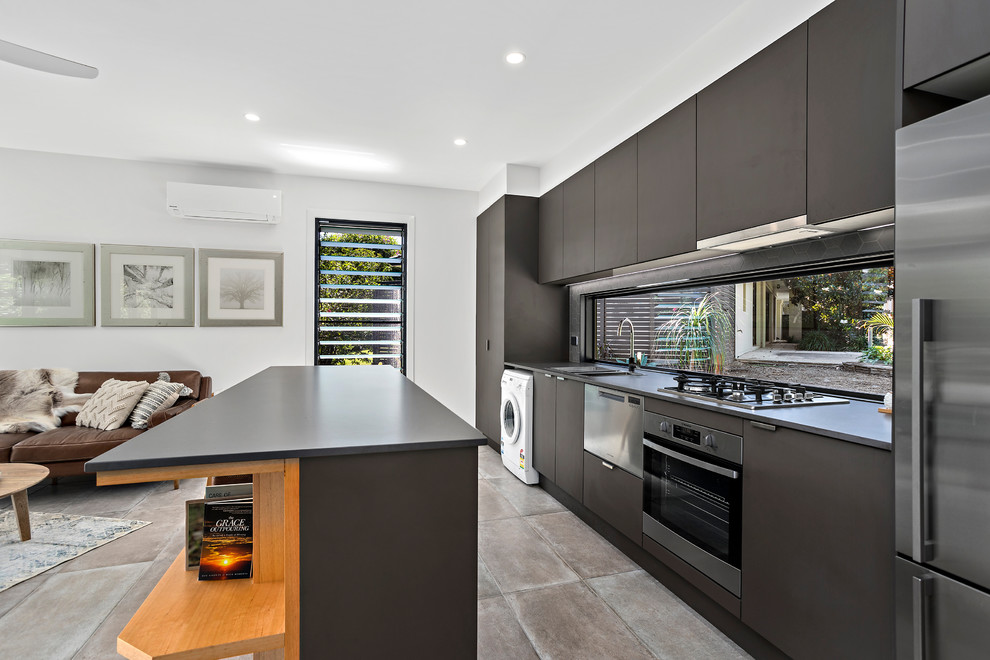 Design ideas for a small beach style galley open plan kitchen in Other with a drop-in sink, flat-panel cabinets, window splashback, stainless steel appliances, with island, black benchtop, grey cabinets, quartz benchtops, grey splashback, ceramic floors and beige floor.