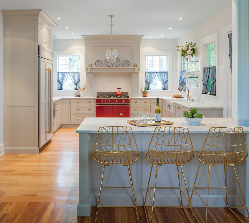 Large transitional u-shaped eat-in kitchen in New York with a farmhouse sink, light hardwood floors, a peninsula, recessed-panel cabinets, white cabinets, marble benchtops, white splashback, subway tile splashback, panelled appliances and brown floor.