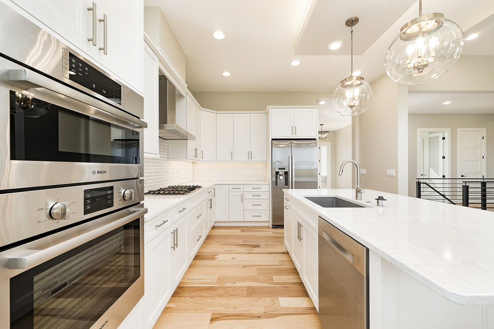 Inspiration for a transitional l-shaped kitchen in Other with an undermount sink, recessed-panel cabinets, white cabinets, white splashback, stainless steel appliances, light hardwood floors, with island, beige floor and white benchtop.