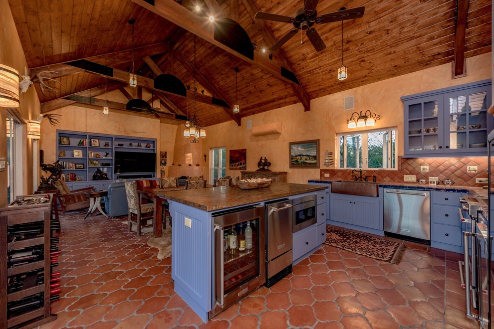 Photo of a mid-sized u-shaped open plan kitchen in Austin with an undermount sink, flat-panel cabinets, blue cabinets, tile benchtops, brown splashback, terra-cotta splashback, stainless steel appliances, terra-cotta floors, with island and brown floor.