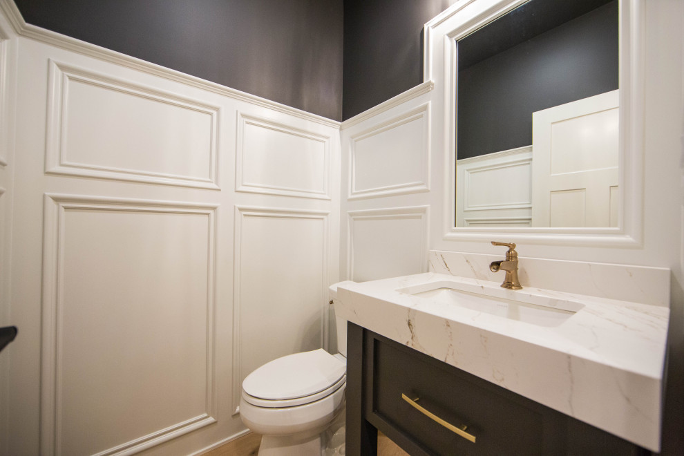 Inspiration for a medium sized traditional cloakroom in Indianapolis with recessed-panel cabinets, black cabinets, a two-piece toilet, black walls, laminate floors, a submerged sink, quartz worktops, brown floors, white worktops, a freestanding vanity unit and panelled walls.