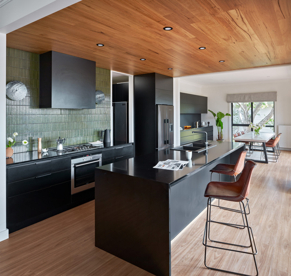 Foto på ett stort funkis svart kök och matrum, med en dubbel diskho, svarta skåp, bänkskiva i kvarts, grönt stänkskydd, stänkskydd i keramik, rostfria vitvaror, ljust trägolv, en köksö och brunt golv