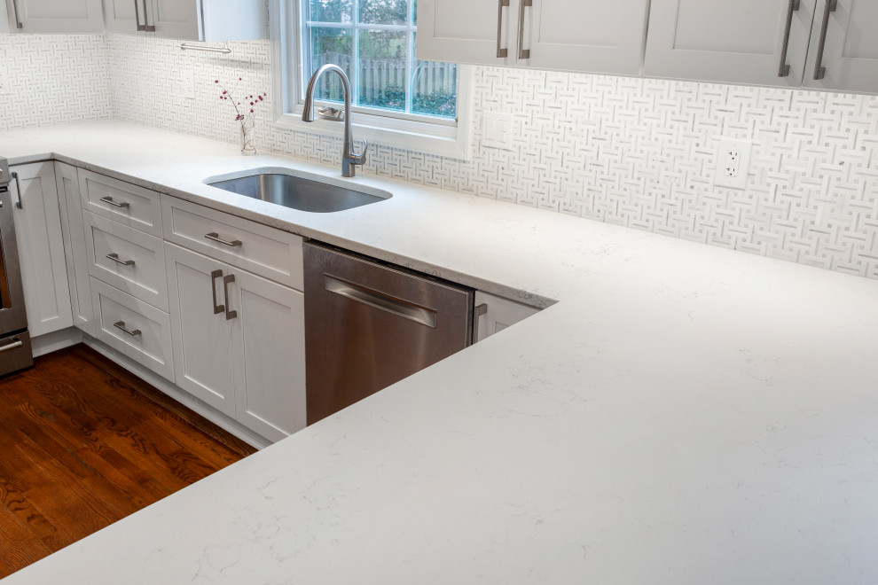 Medium sized traditional l-shaped kitchen in DC Metro with a submerged sink, shaker cabinets, white cabinets, engineered stone countertops, white splashback, marble splashback, stainless steel appliances, medium hardwood flooring, a breakfast bar, brown floors and white worktops.