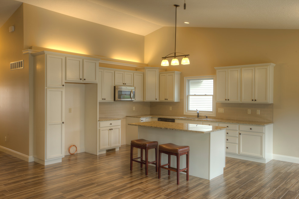 Open concept kitchen - mid-sized transitional l-shaped light wood floor and beige floor open concept kitchen idea in Chicago with an undermount sink, recessed-panel cabinets, white cabinets, granite countertops, beige backsplash, subway tile backsplash, stainless steel appliances and an island