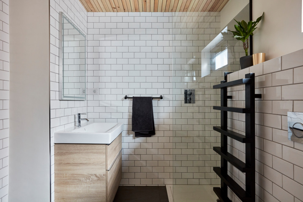 Photo of a small contemporary 3/4 bathroom in London with a drop-in tub, a corner shower, a one-piece toilet, white tile, ceramic tile, white walls, slate floors, a trough sink, grey floor, an open shower, a single vanity, a freestanding vanity, timber, flat-panel cabinets, light wood cabinets and white benchtops.