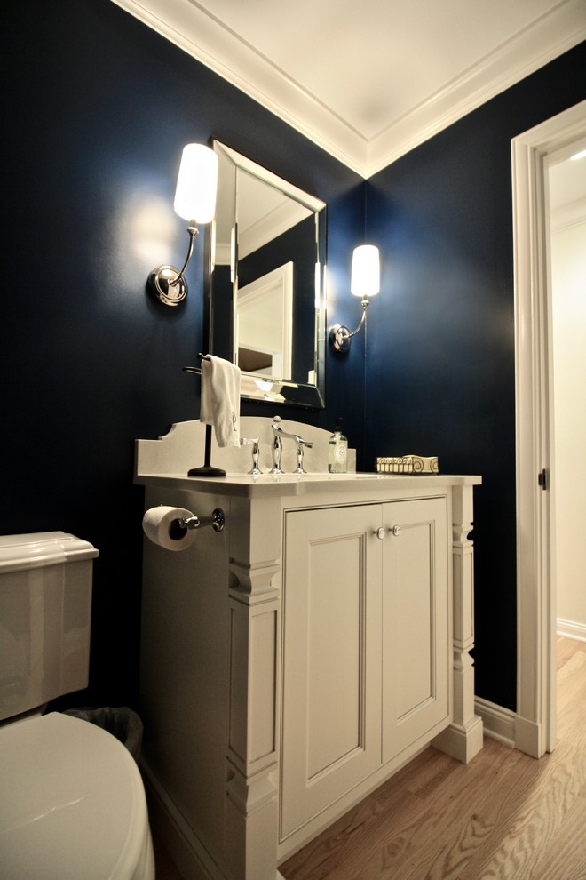 Inspiration for a mid-sized transitional powder room in St Louis with recessed-panel cabinets, white cabinets, a two-piece toilet, blue walls, light hardwood floors, an undermount sink and engineered quartz benchtops.