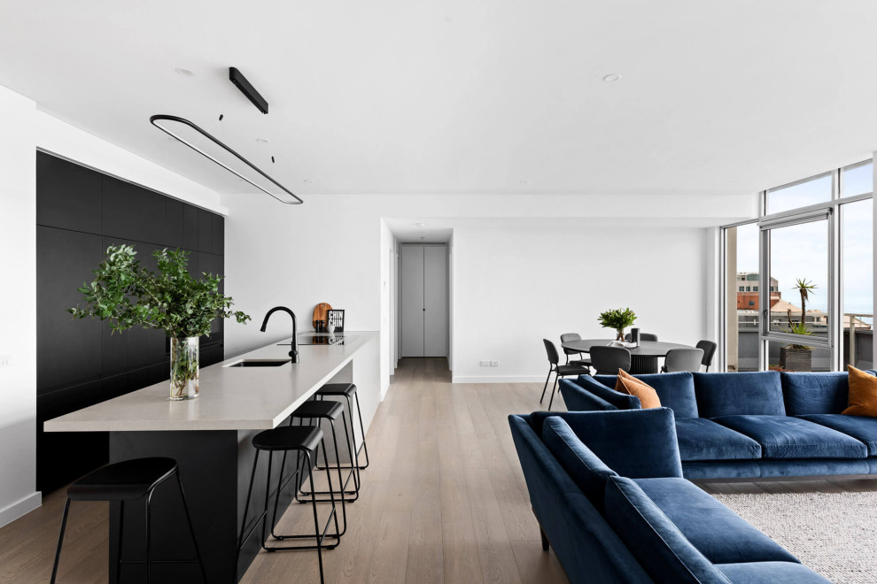 This is an example of a medium sized contemporary single-wall open plan kitchen in Melbourne with a submerged sink, flat-panel cabinets, black cabinets, concrete worktops, black appliances, medium hardwood flooring, an island, brown floors and grey worktops.